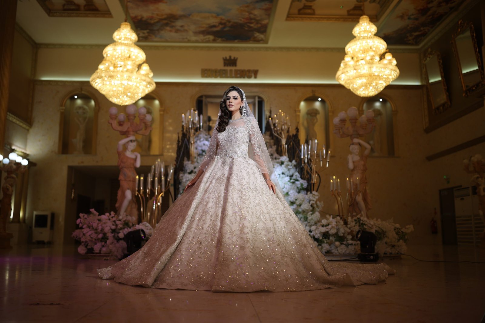 Bride in the grand hall beneath crystal chandeliers at The Excellency